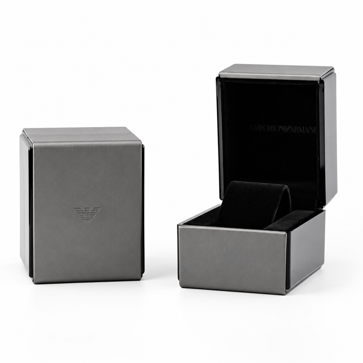 An open and closed dark gray watch box on a white background. The closed box features a subtle embossed logo on the front, while the open box reveals a black velvet interior and the brand name 'EMPORIO ARMANI' printed inside the lid.